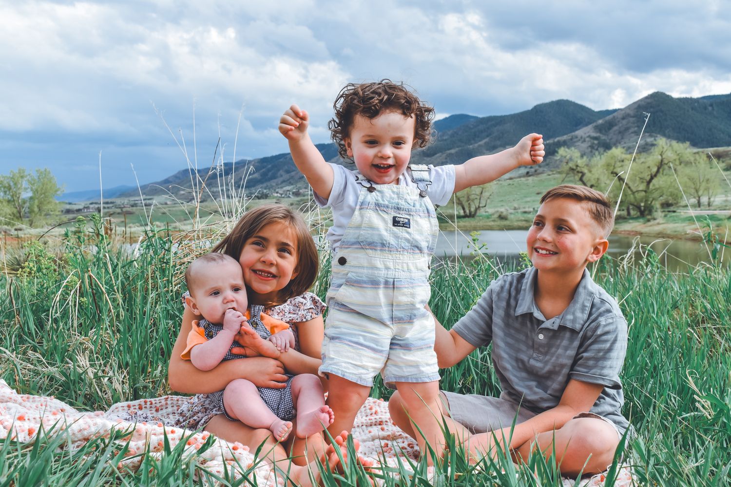 Four children in matching black tops pose together among pine trees in a natural outdoor forest setting.
