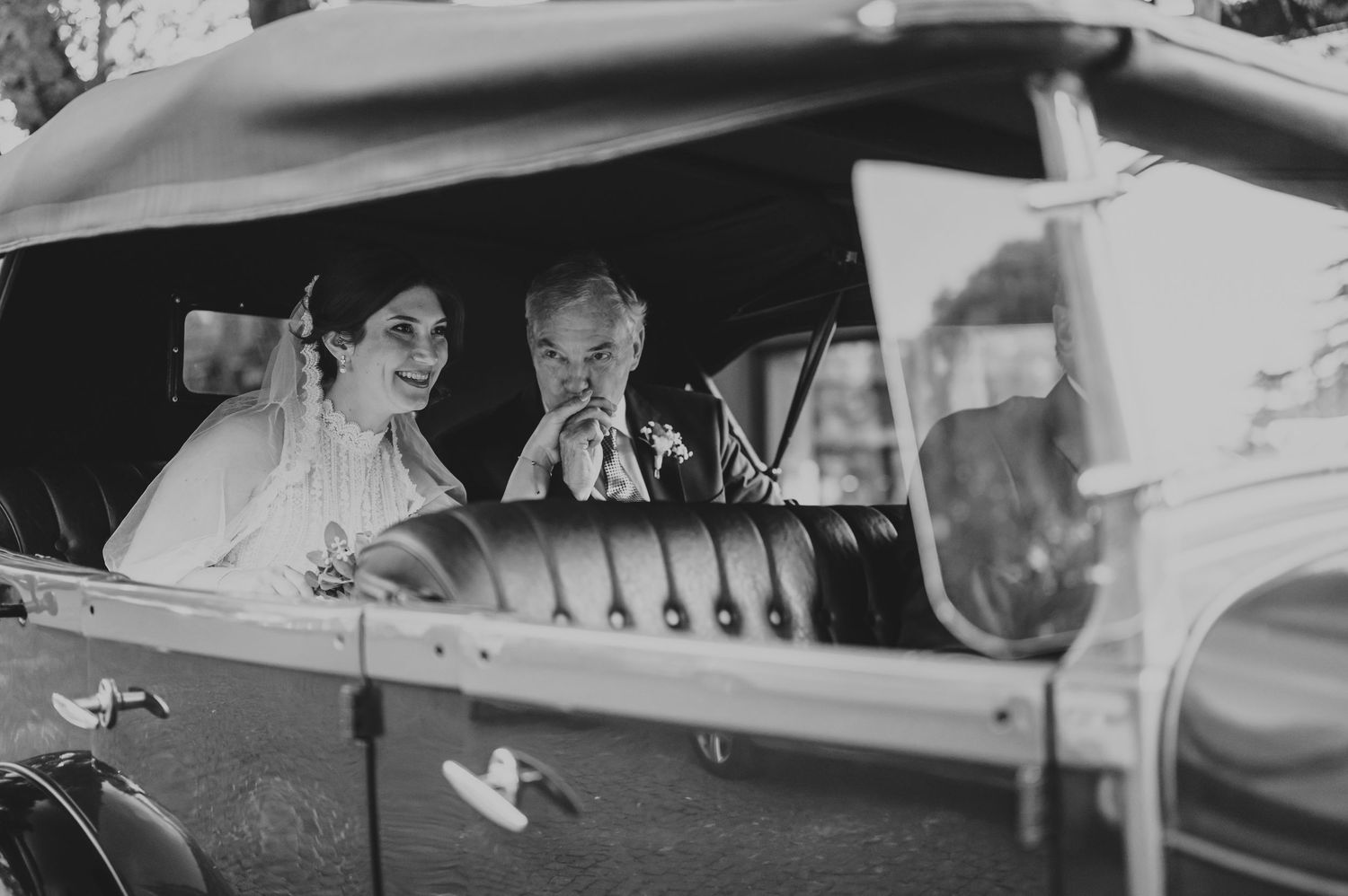 Black and white photo of bride and companion sharing a moment inside a vintage classic car.