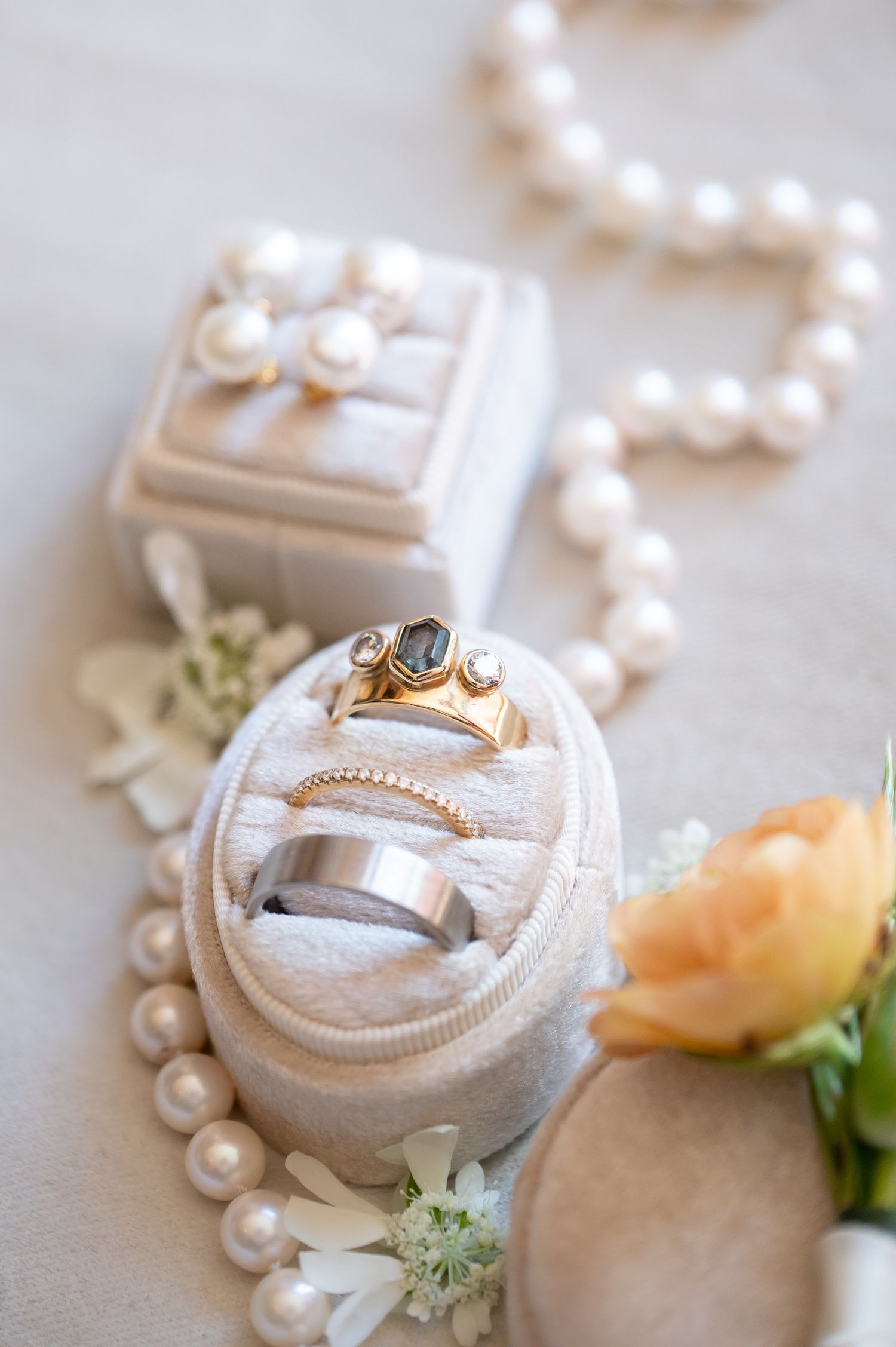 Elegant wedding rings and pearl earrings displayed in velvet jewelry boxes beside a pearl necklace and peach rose for Vail elopement