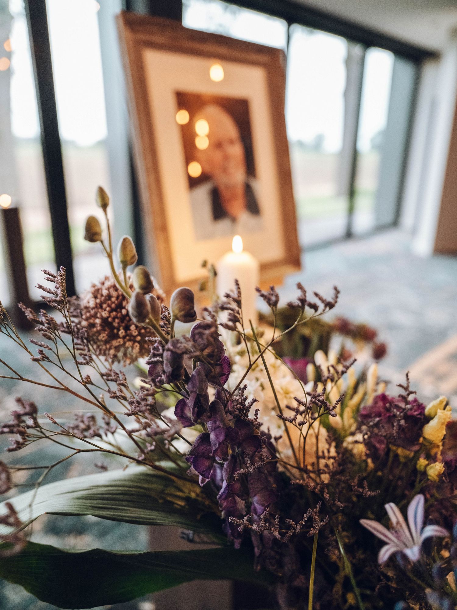 Memorial display with purple flowers, candle, and framed portrait photo at a funeral service.