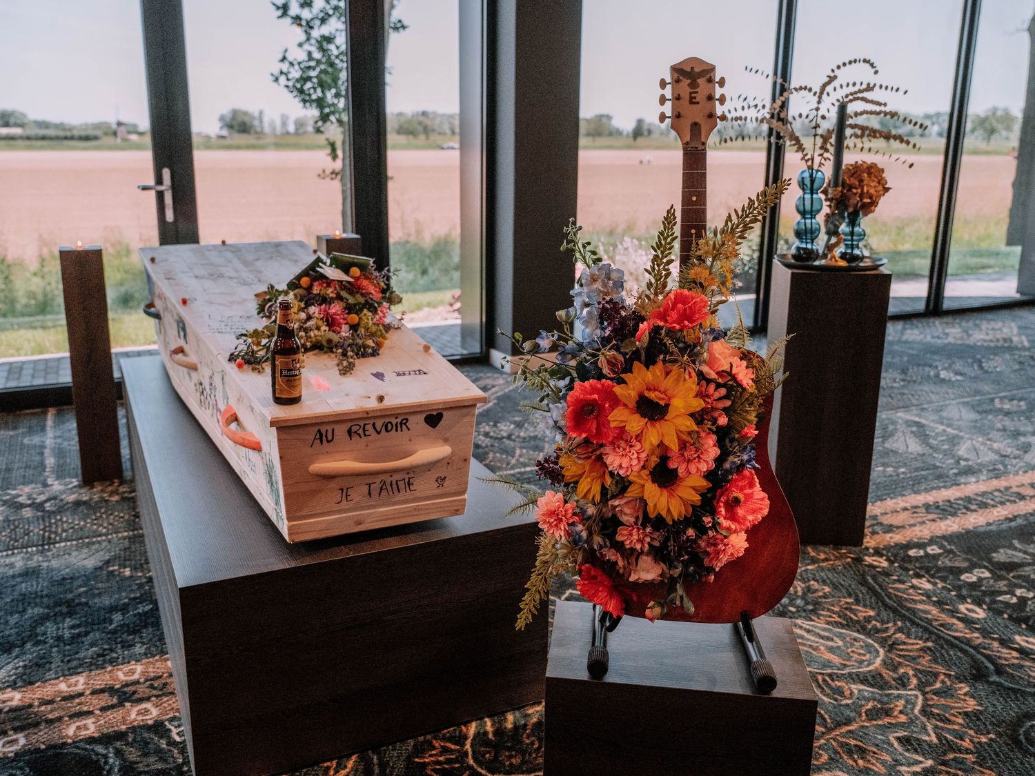 Funeral tribute display with a decorated casket, guitar covered in colorful flowers, and sunflowers.