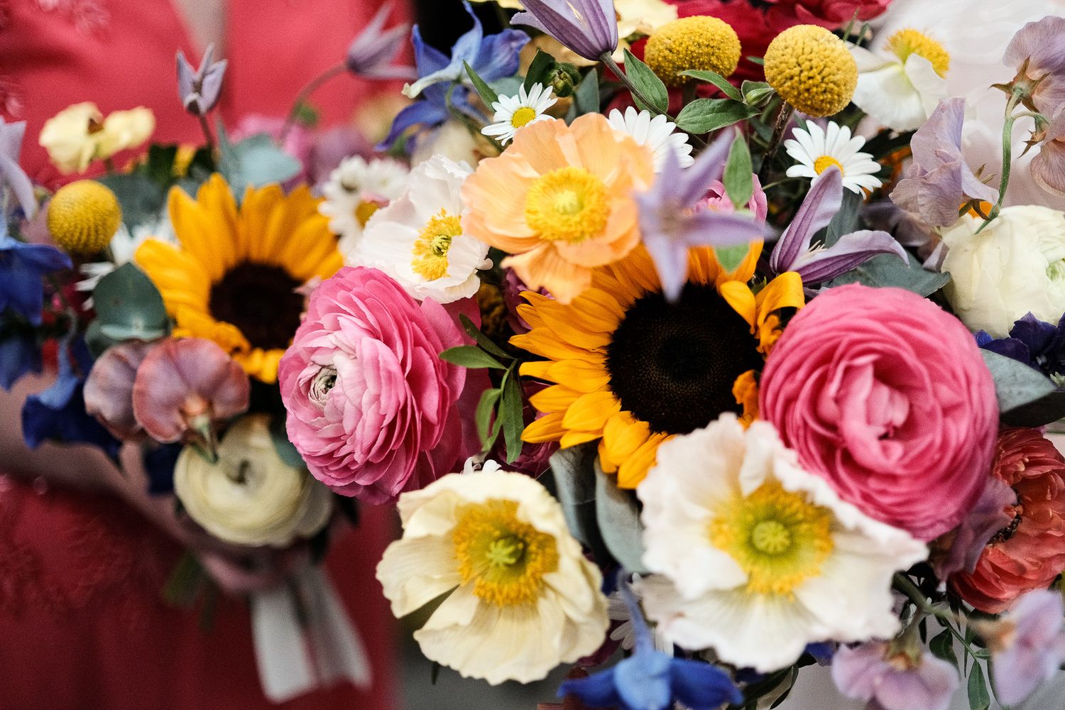 Colourful wedding bouquets featuring sunflowers, pink ranunculus, white poppies, and mixed wildflowers held by bridesmaids.