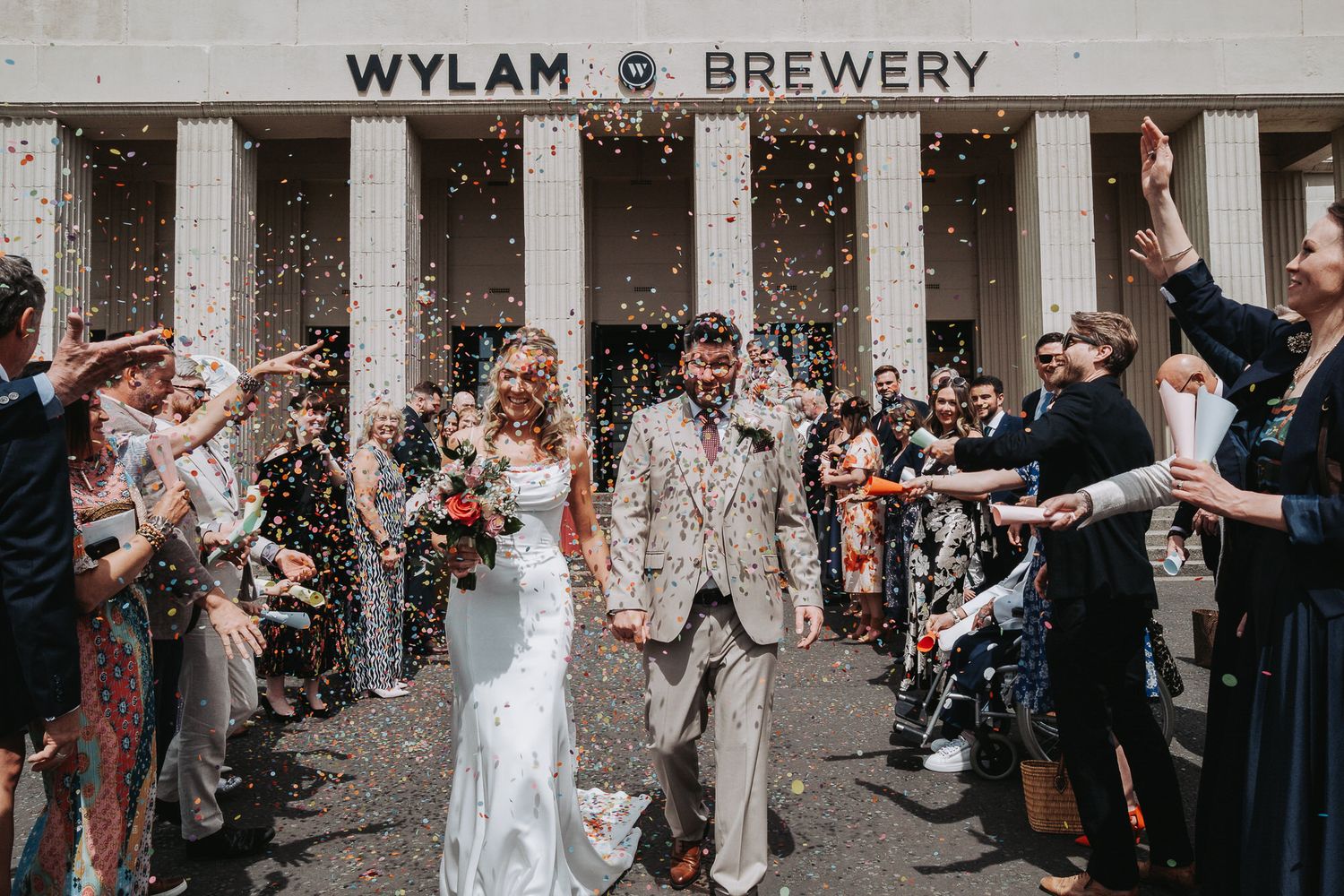 Newlyweds celebrate with confetti outside Wylam Brewery, surrounded by cheering guests on their wedding day.