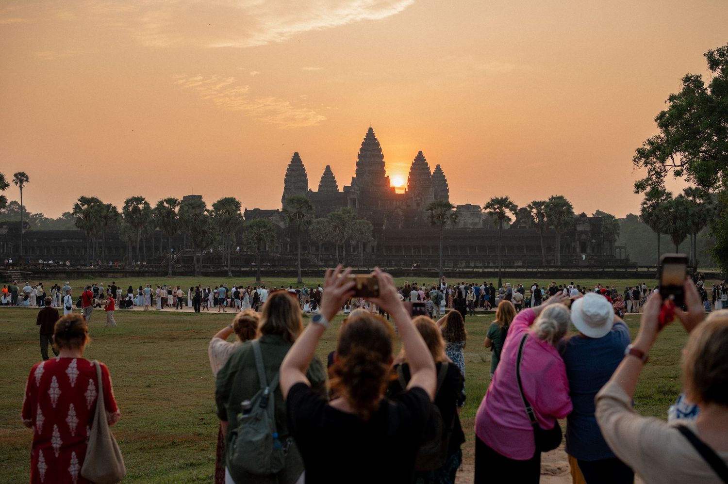Crowds of tourists photograph the stunning sunrise over Angkor Wat temple complex in Cambodia at dawn.