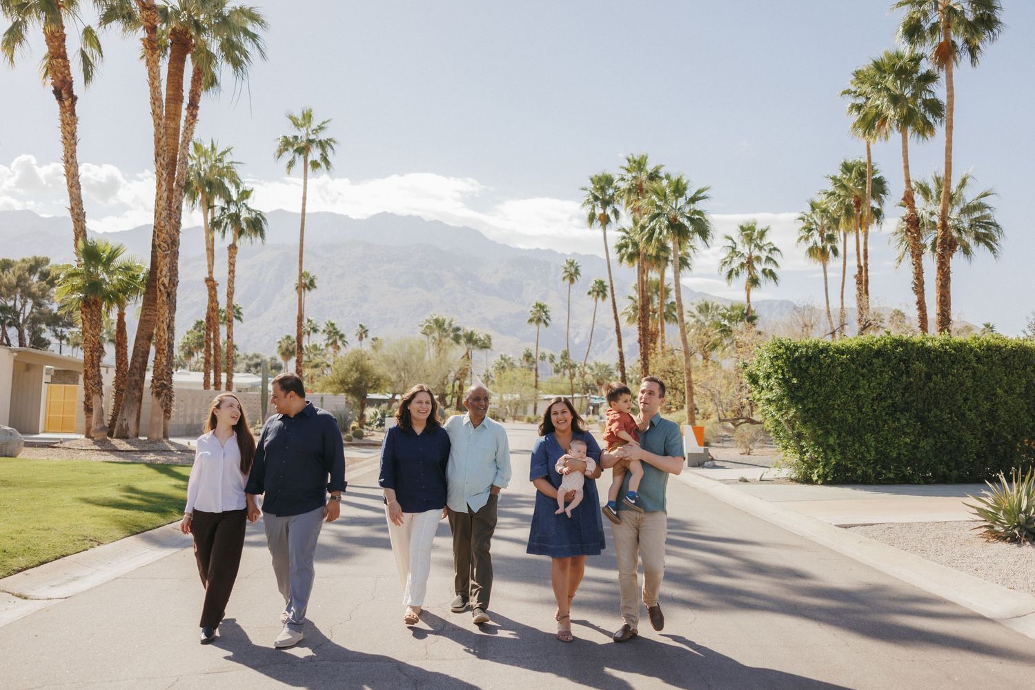 Family of three embracing by a luxurious outdoor pool with palm trees and mountain views in Palm Springs.