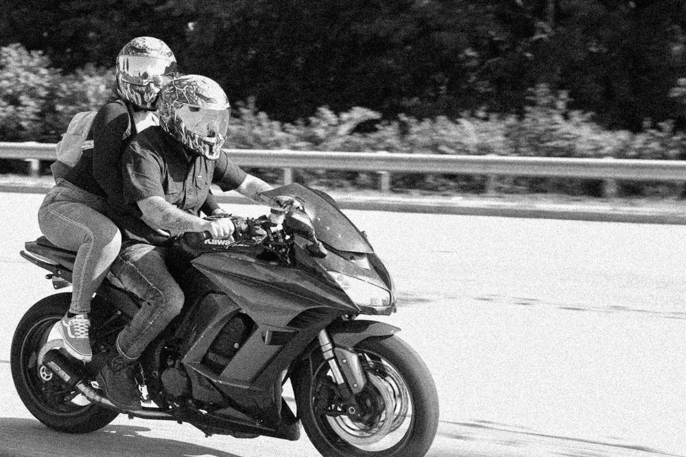 Two riders on a sport motorcycle cruising on a highway in black and white photography.