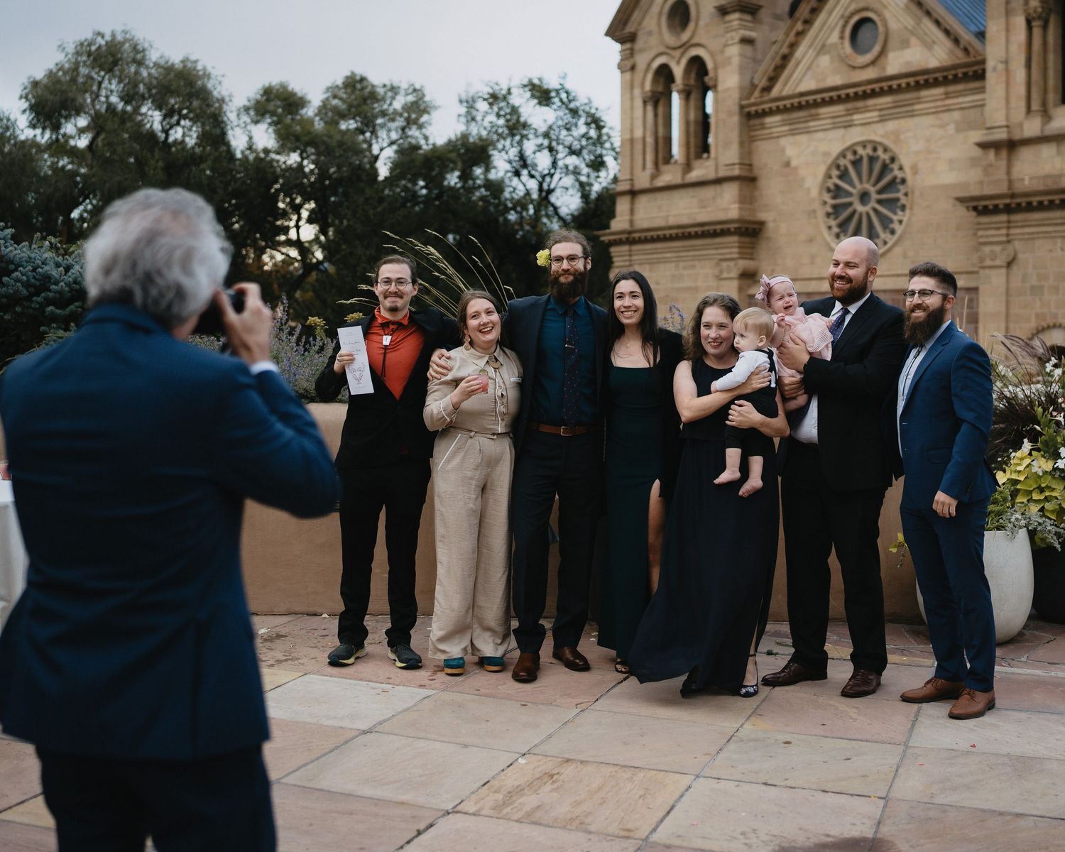 A photographer captures a group of elegantly dressed family members posing outside a historic church at dusk.
