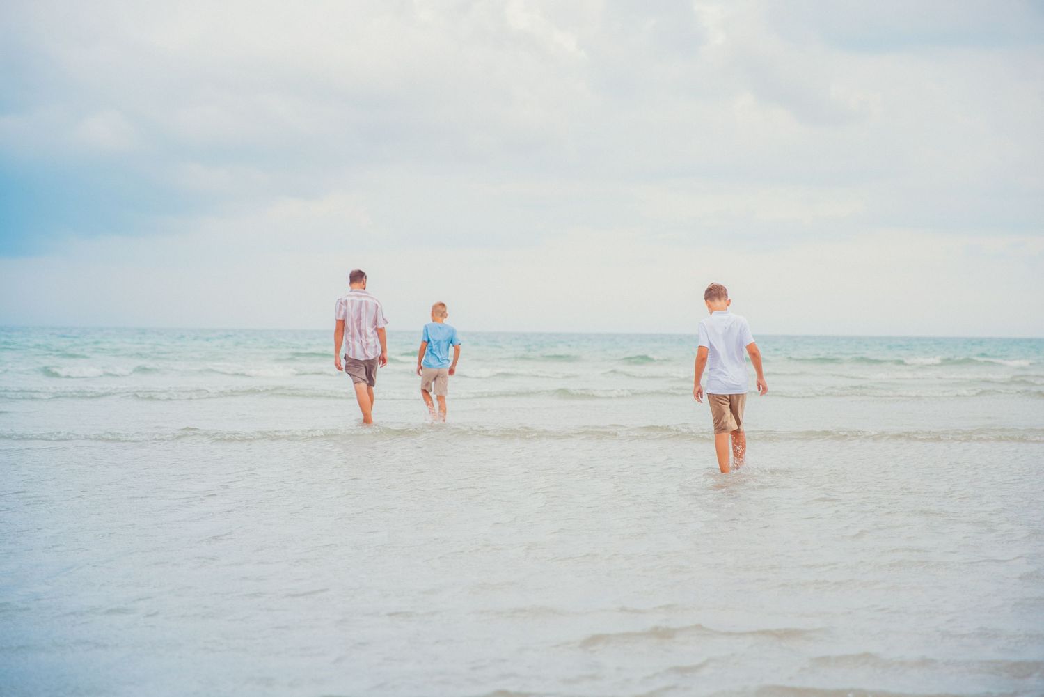 A documentary style picture of a dad with two boys walking in shallow water at the beach