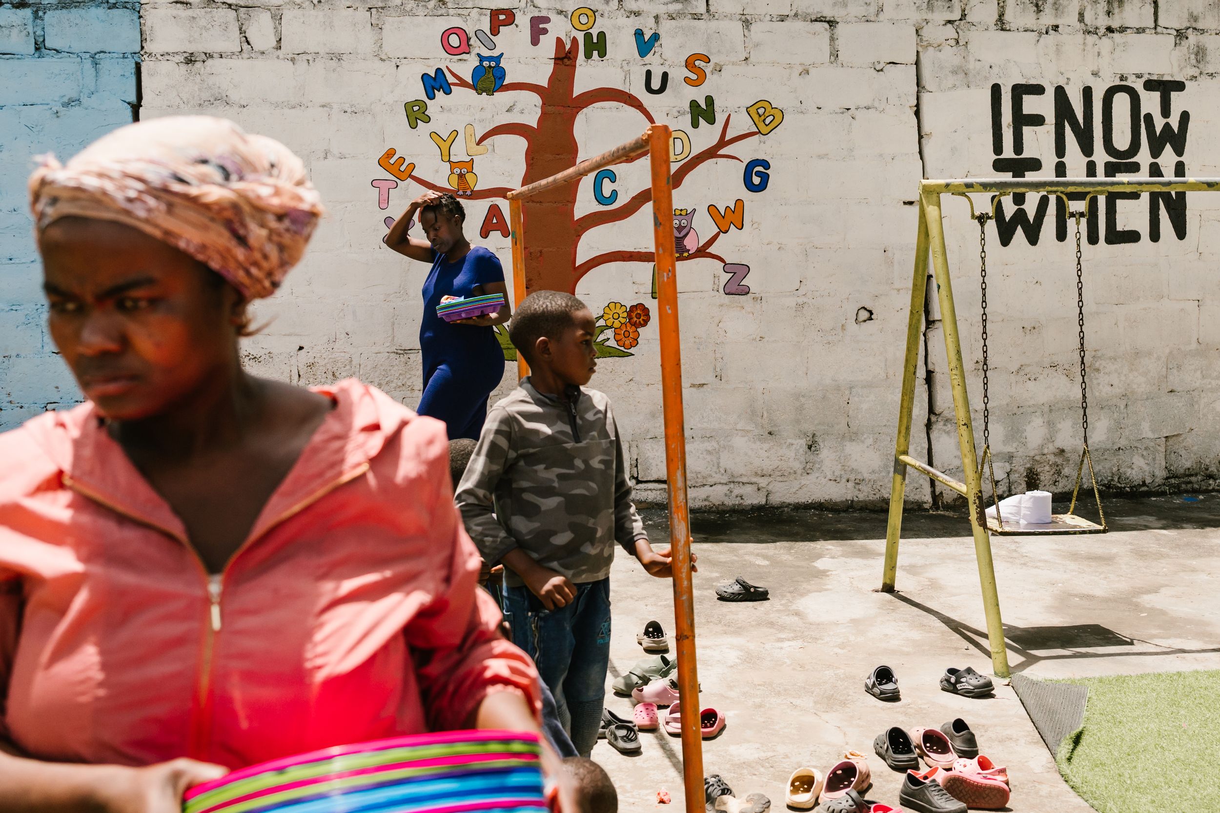 Women and children in an urban outdoor space with colorful murals and a swing set in what appears to be Africa.