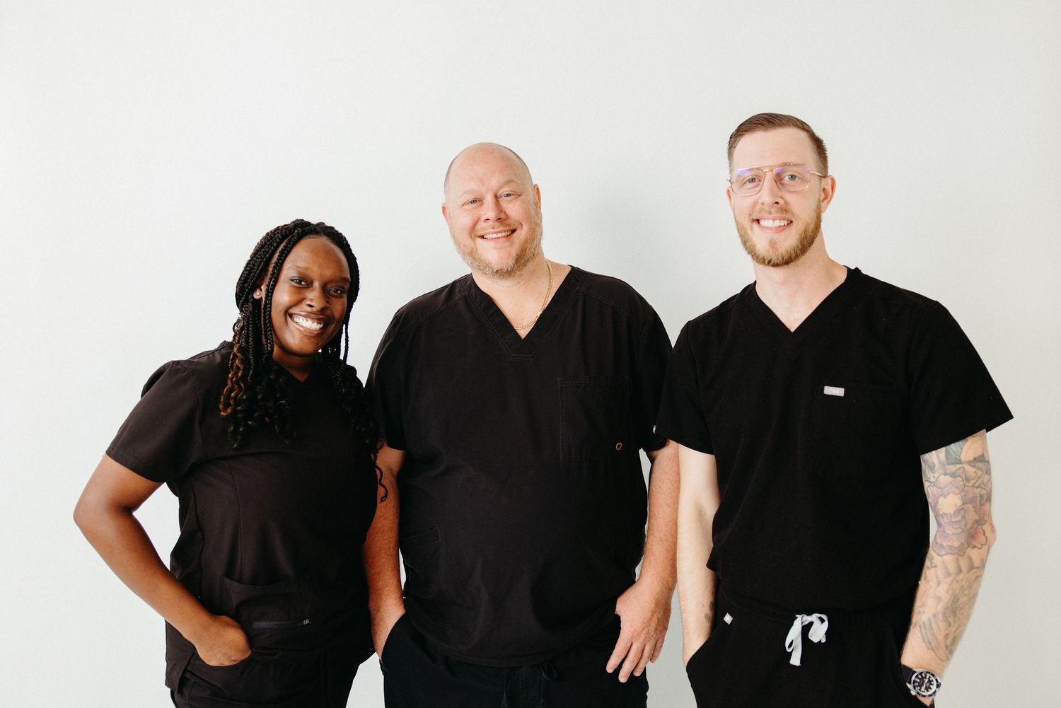 Three healthcare professionals in black scrubs smiling together against a white background.