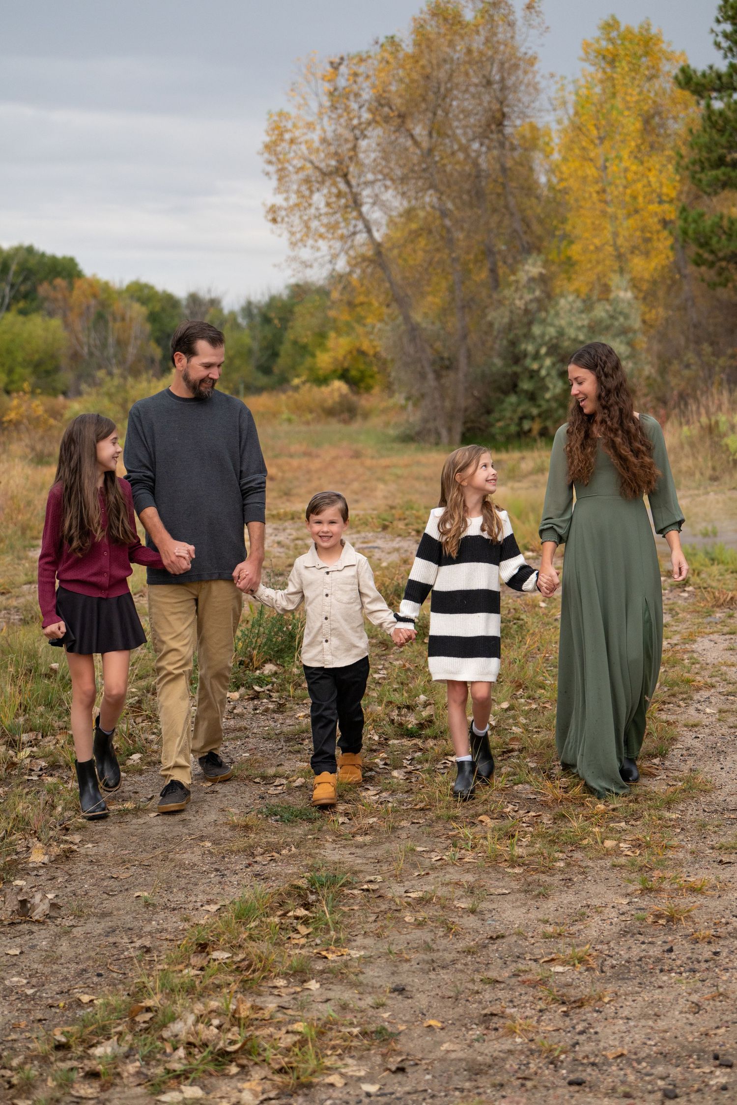 Family of five walking hand-in-hand on a nature path surrounded by autumn foliage trees.