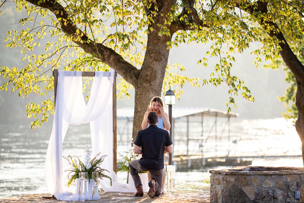 Man on one knee proposing under an autumn tree at a lakeside surprise proposal in Mountain Home, Arkansas