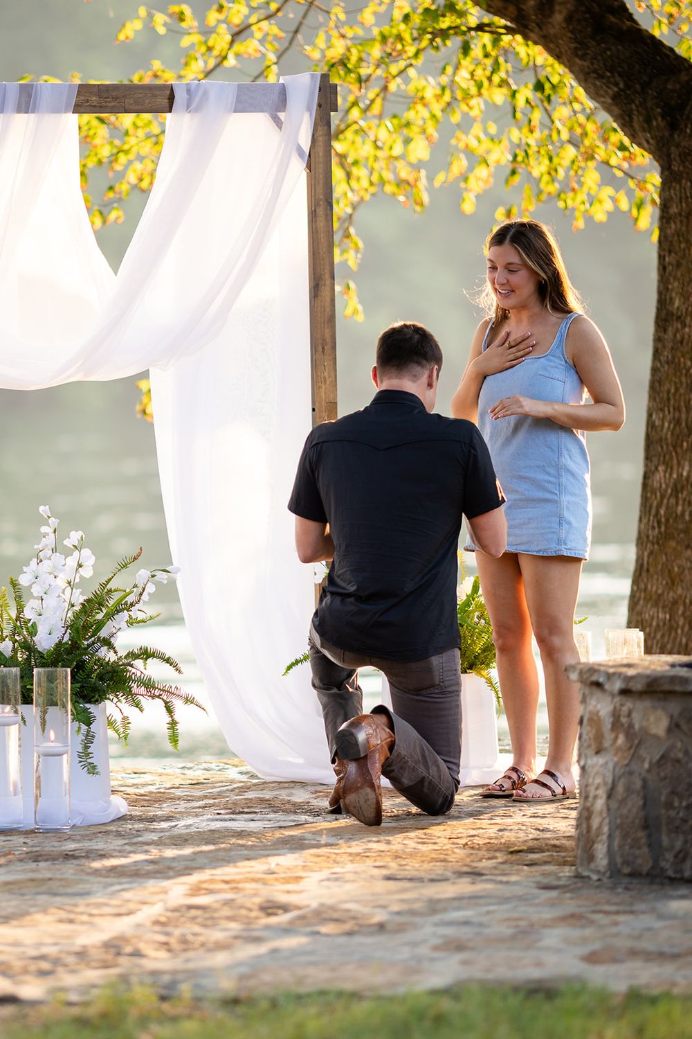 Riverside surprise proposal on the White River in Mountain Home, Arkansas, as a man kneels by a white draped arch