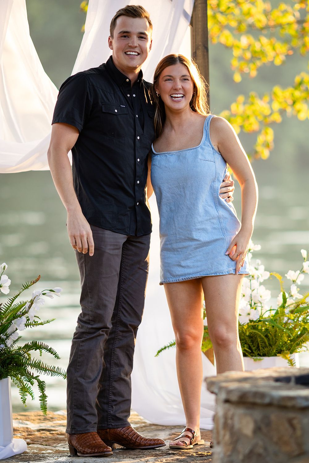 Just-engaged couple smiling together beside a white curtain arch after a surprise proposal on the White River in Mountain Home, Arkansas