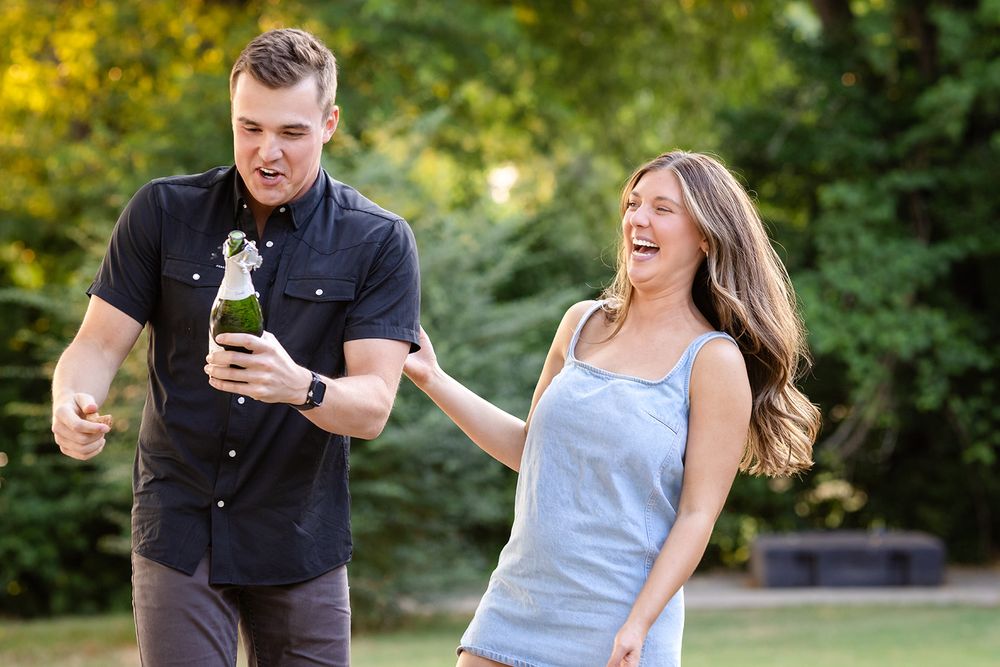 Just-engaged couple laughing as they pop champagne to celebrate their engagement in Mountain Home, Arkansas