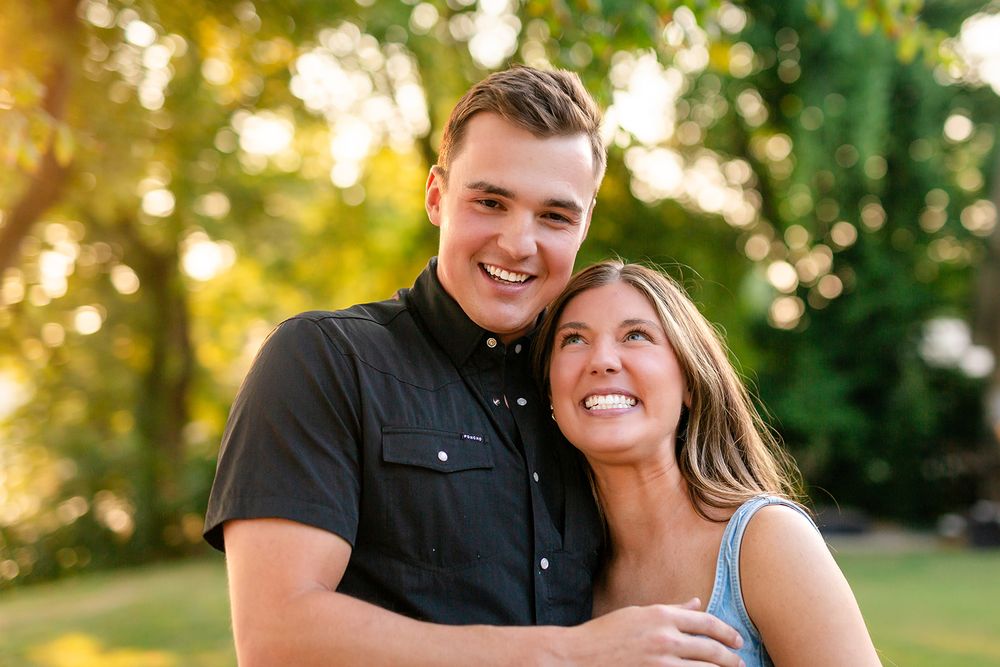 Newly engaged couple smiling cheek to cheek in golden evening light in Mountain Home, Arkansas