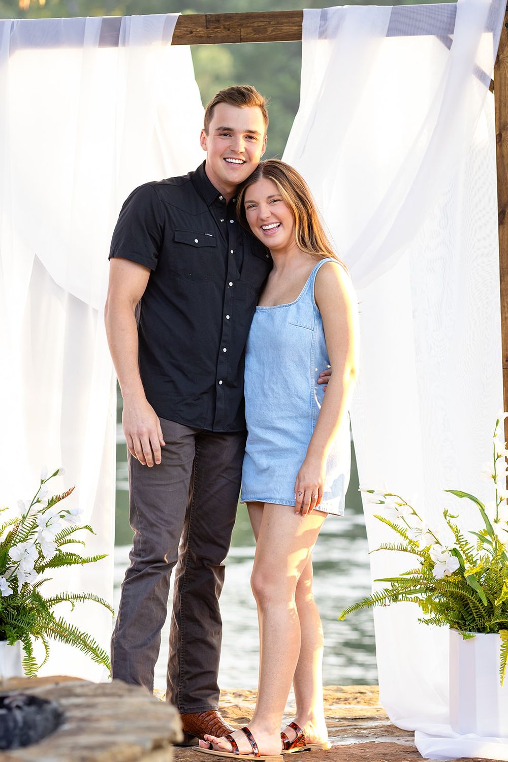 Just-engaged couple standing together by a white draped arch on the White River in Mountain Home, Arkansas