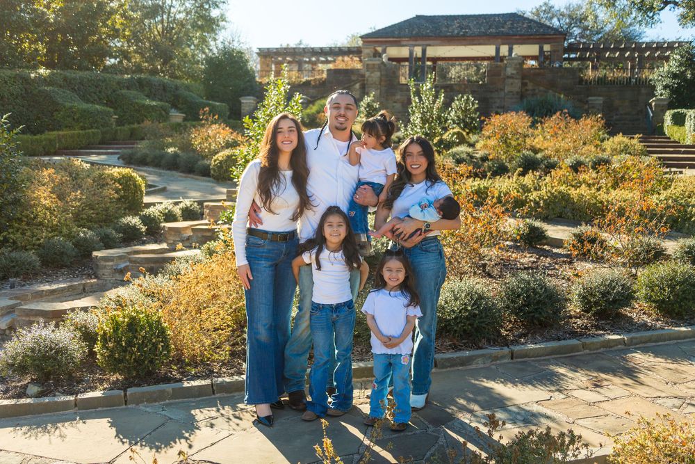 Family of six poses in a sunny garden with lush greenery and stone pathways.