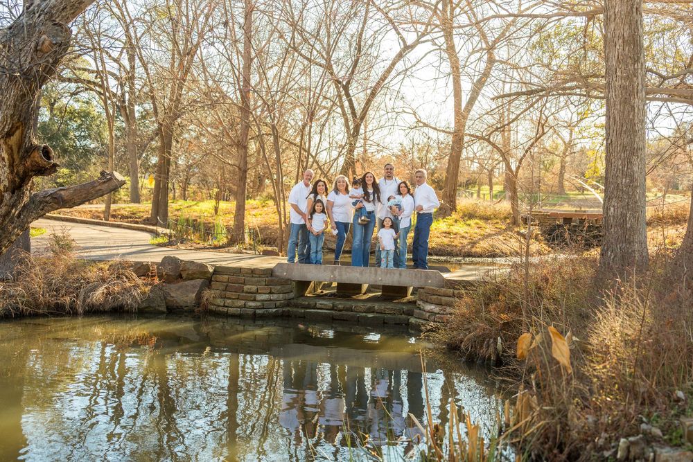 Family group posing on a stone bridge over a pond in a park with bare trees and golden light.