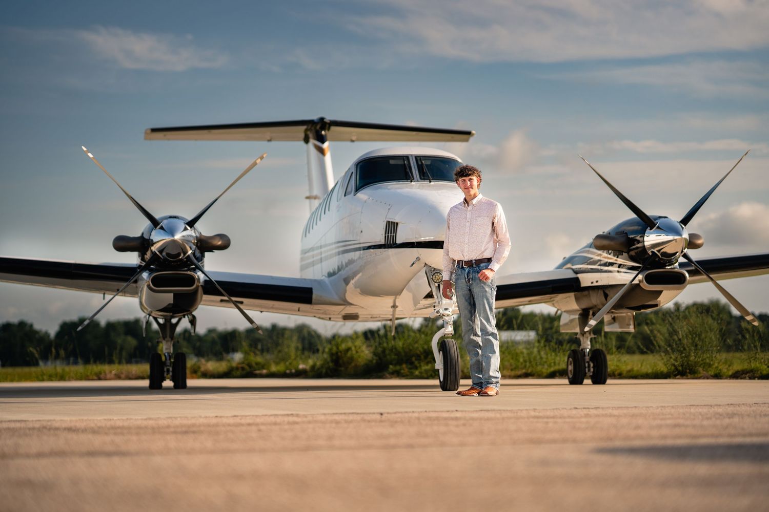 Man standing in front of a twin-engine turboprop aircraft on a runway at sunset.
