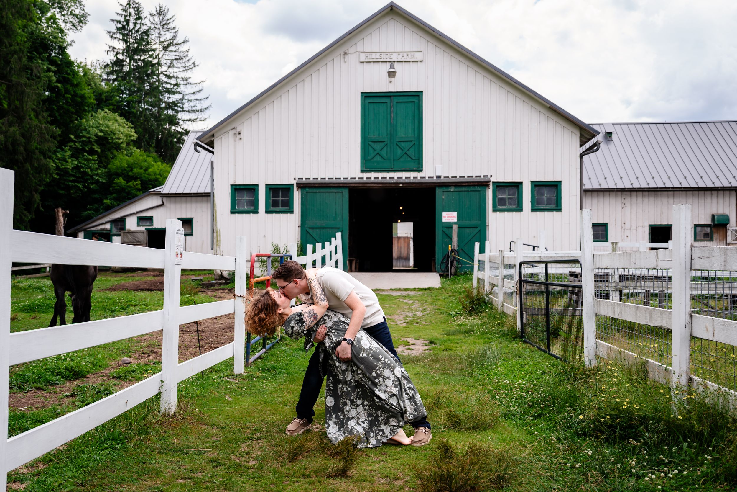 Couple sharing a romantic dip kiss outside a white barn with green doors at a rustic farm wedding venue.