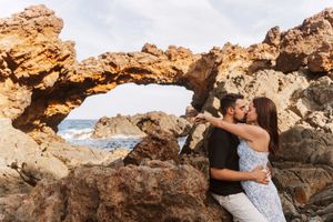 Couple kissing romantically through natural rock arch formation by ocean coastline.