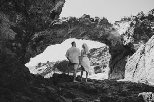 Couple standing together in a rocky sea cave arch, black and white romantic coastal photography.