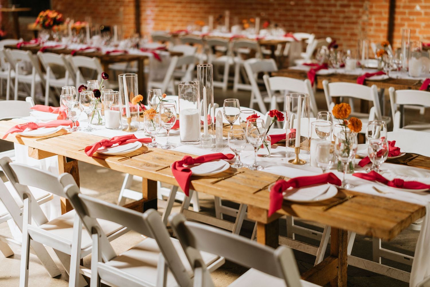 Wooden reception tables set with white plates, red napkins, glassware, and floral details at Seventh Place.