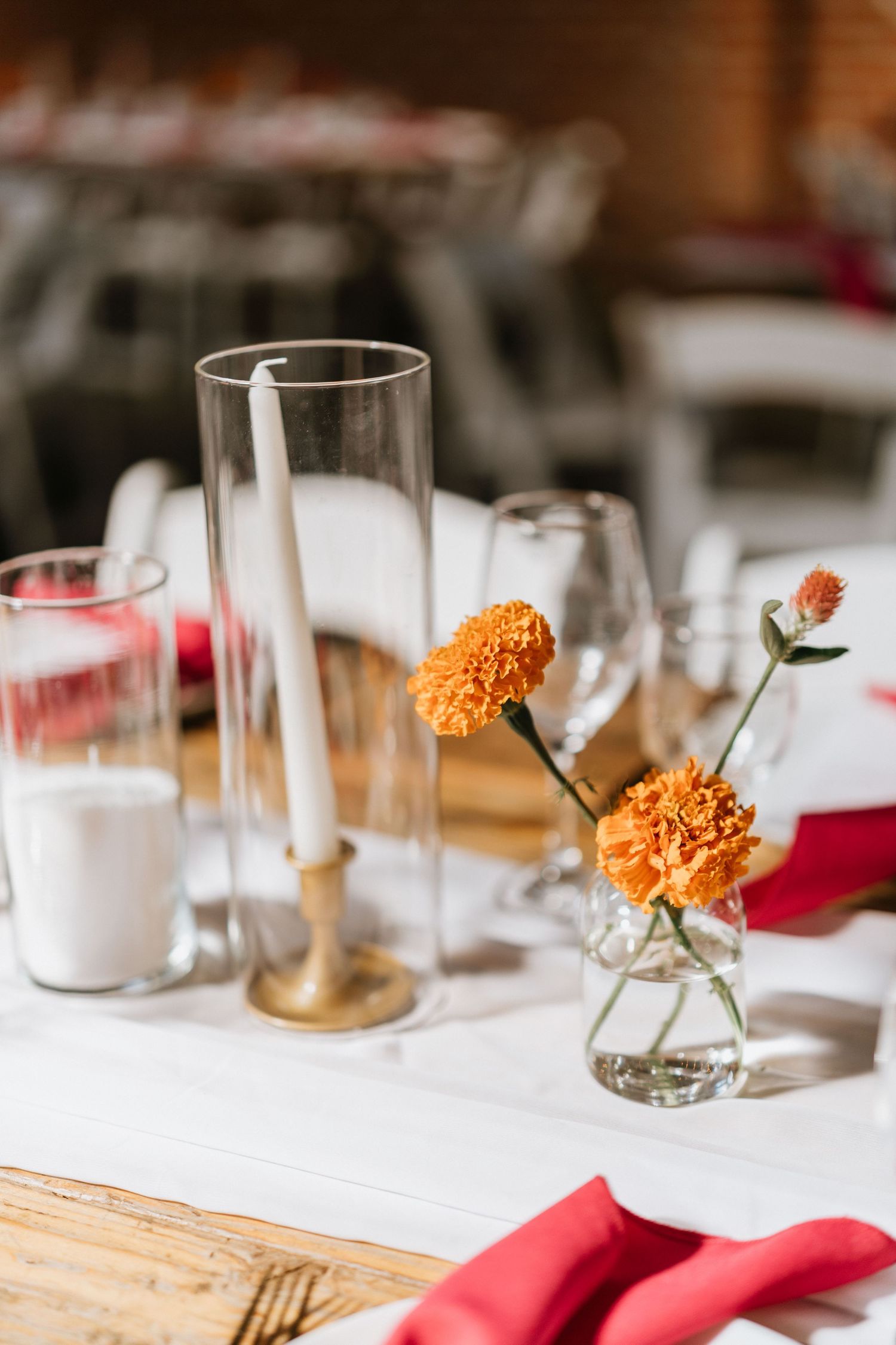 Orange flowers, taper candles, and glassware arranged on a reception table.