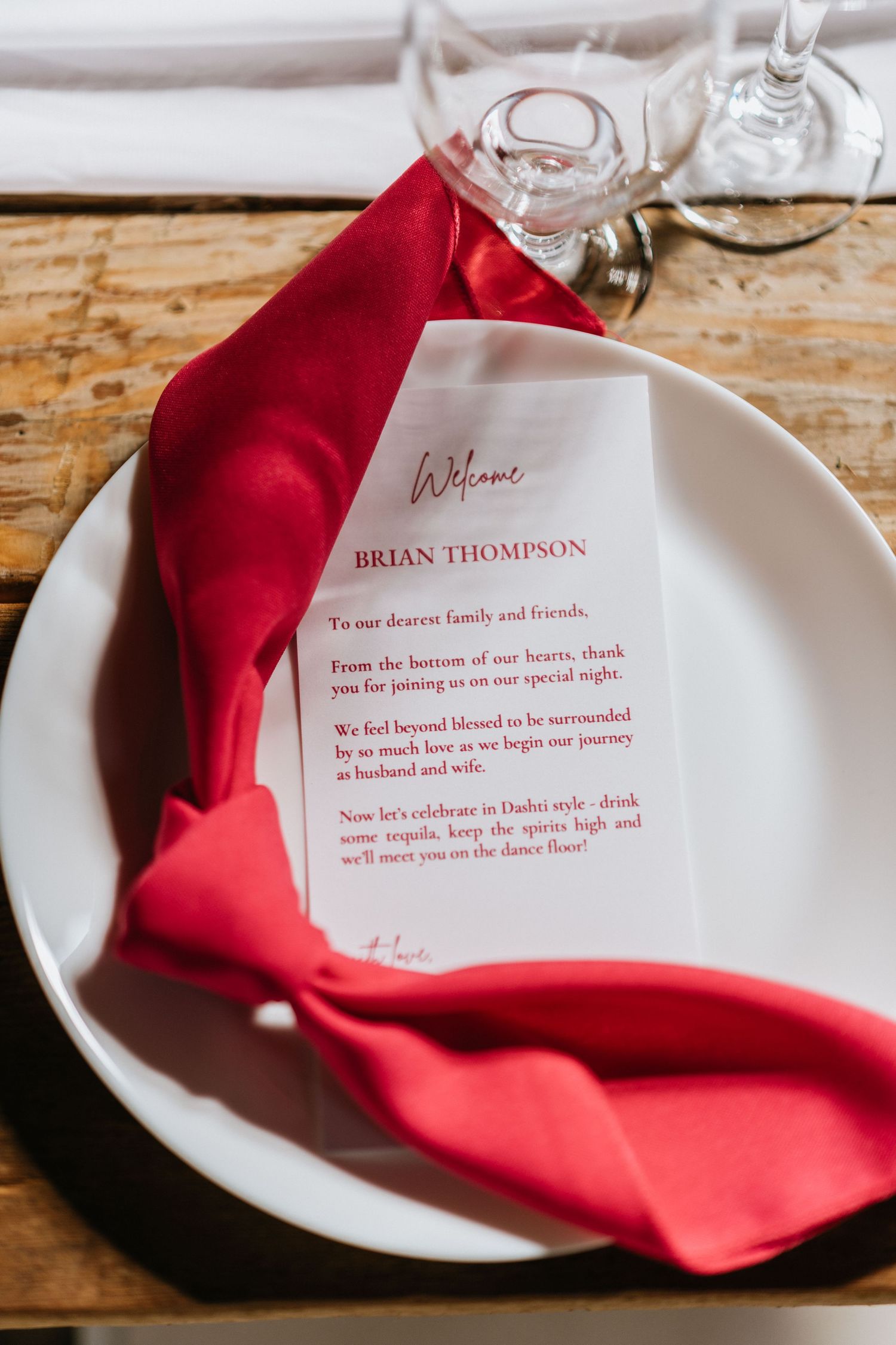 Printed wedding menu displayed on a white plate beneath a red napkin.