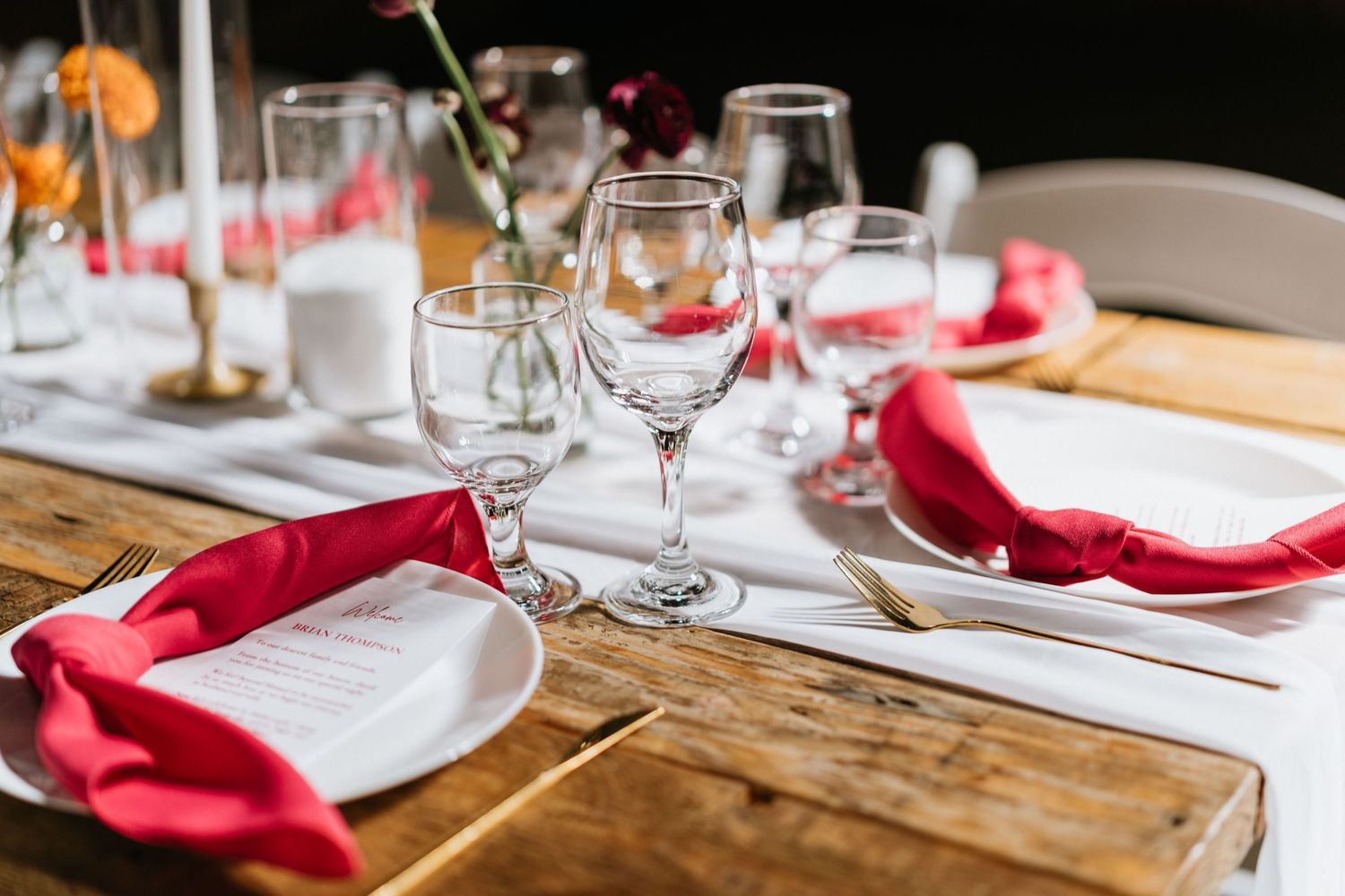 Reception table set with red napkins, clear glassware, candles, and small floral arrangements.