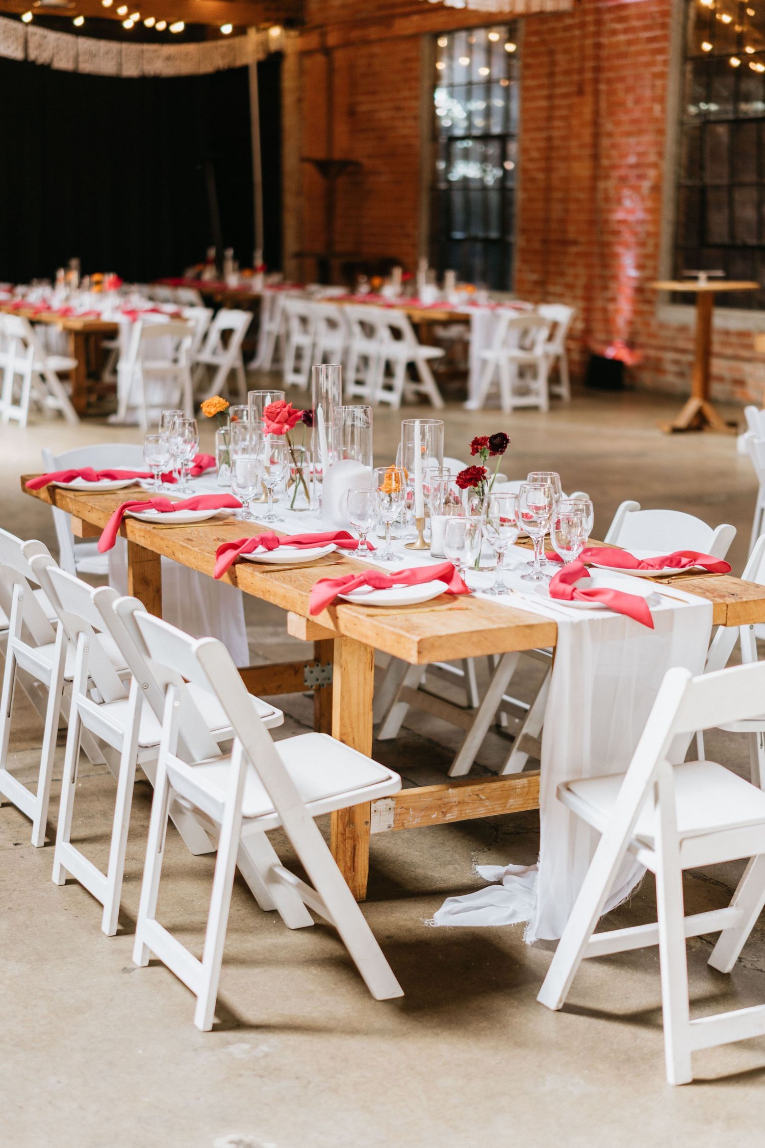 Reception table with white chairs, red napkins, candles, and glassware.