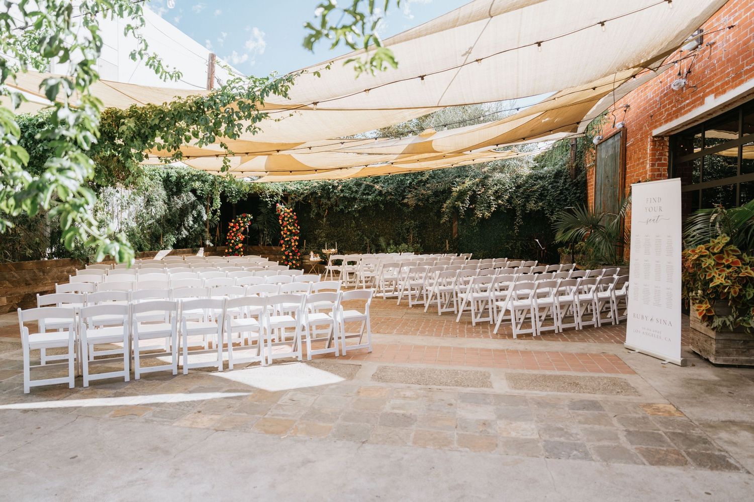 Wide view of the outdoor wedding ceremony space with white chairs beneath fabric canopies at Seventh Place in Los Angeles.