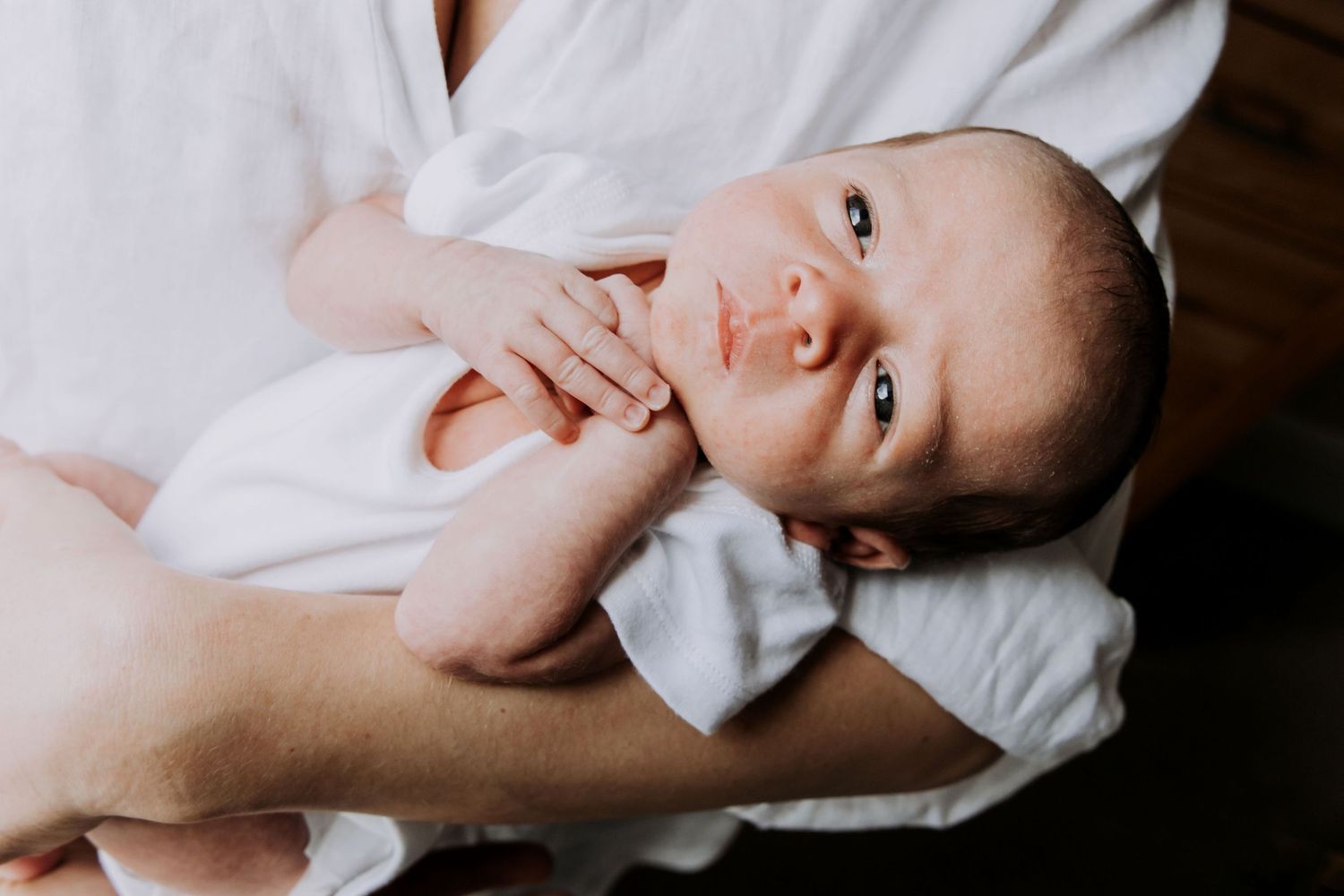 Awake newborn baby looking towards the camera while being gently held during a lifestyle newborn photography session in Cheltenham.