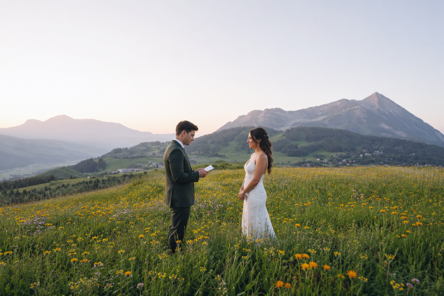 Couple exchanging vows in a wildflower meadow with mountain peaks at sunset during an outdoor elopement.