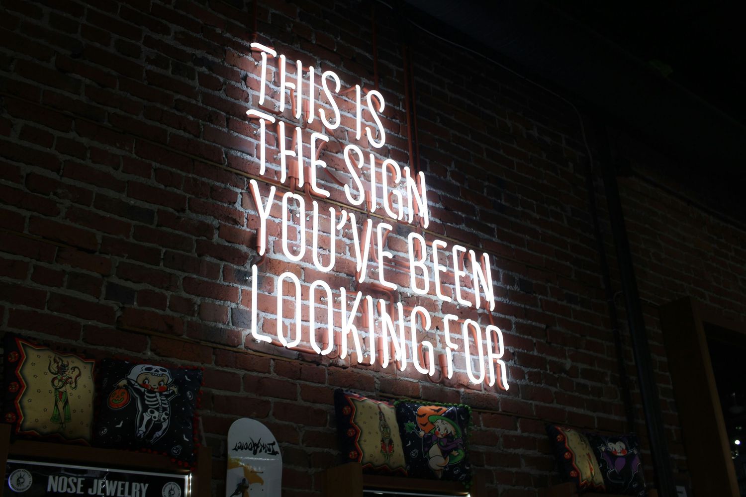Glowing white neon sign on brick wall reading 'This Is The Sign You've Been Looking For' in a bar setting.