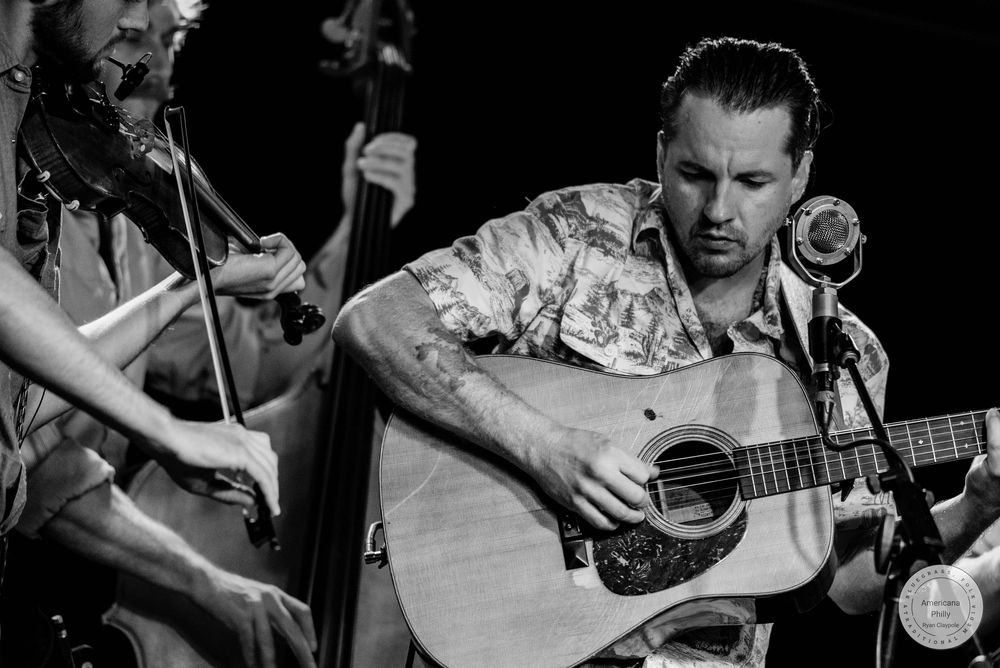 Black and white photo of guitarist and violinist performing together on stage at a live concert.