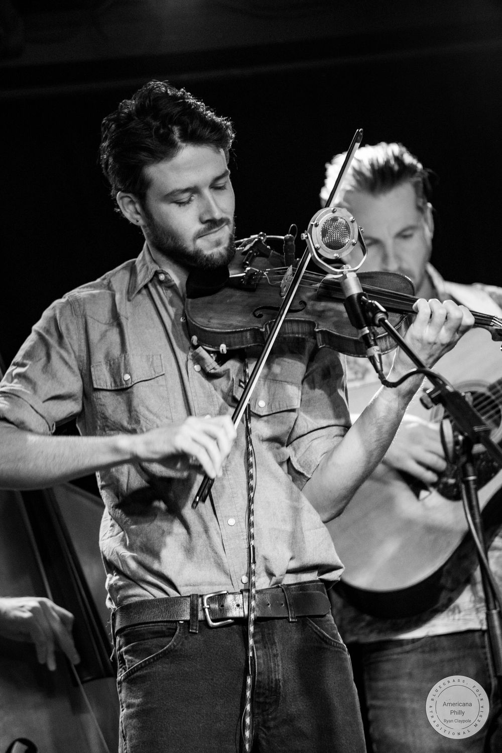 Two musicians playing violins on stage in a black and white performance photo.