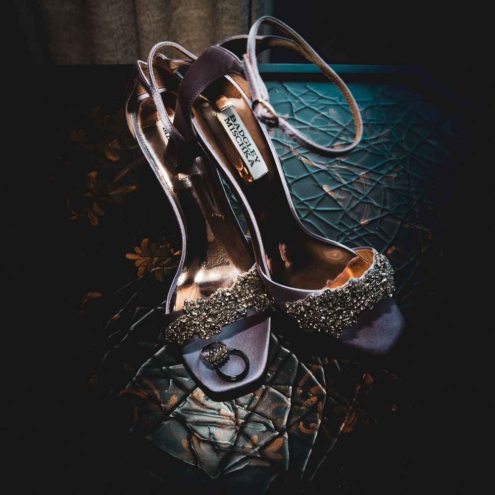 Elegant Badgley Mischka crystal-embellished heels with ankle straps on a decorative blue surface.