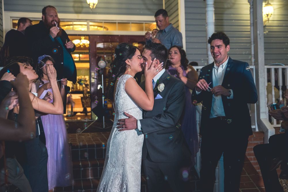 Newlyweds share a joyful first kiss surrounded by cheering guests at outdoor wedding reception.