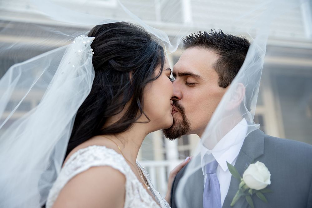 Bride and groom share a romantic kiss under a flowing white veil on their wedding day.