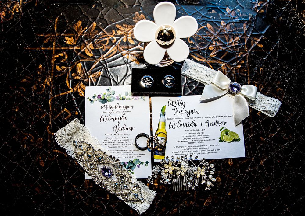 Wedding flat lay with invitations, rings, earrings, garter, and floral accessories on dark textured background.