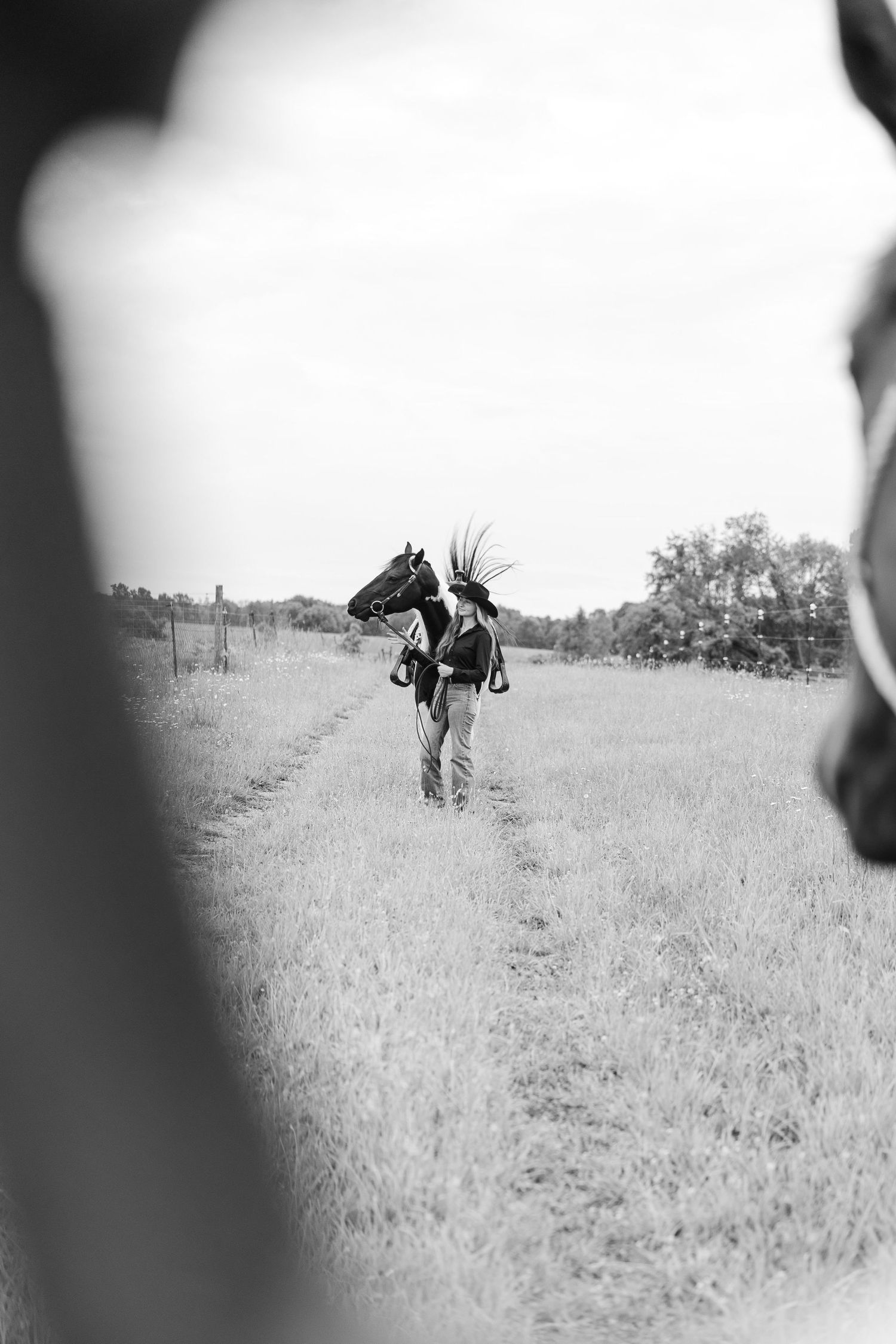 Black and white photo of a person leading a horse through a grassy field along a dirt path.