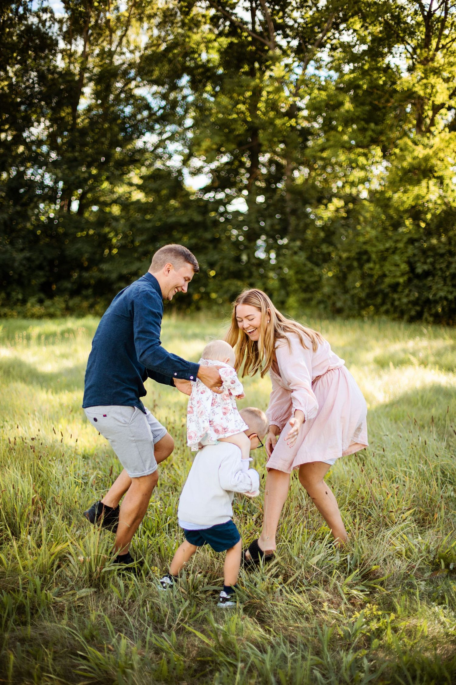 Family enjoying a playful moment together in a sunlit grassy meadow on a warm summer evening.