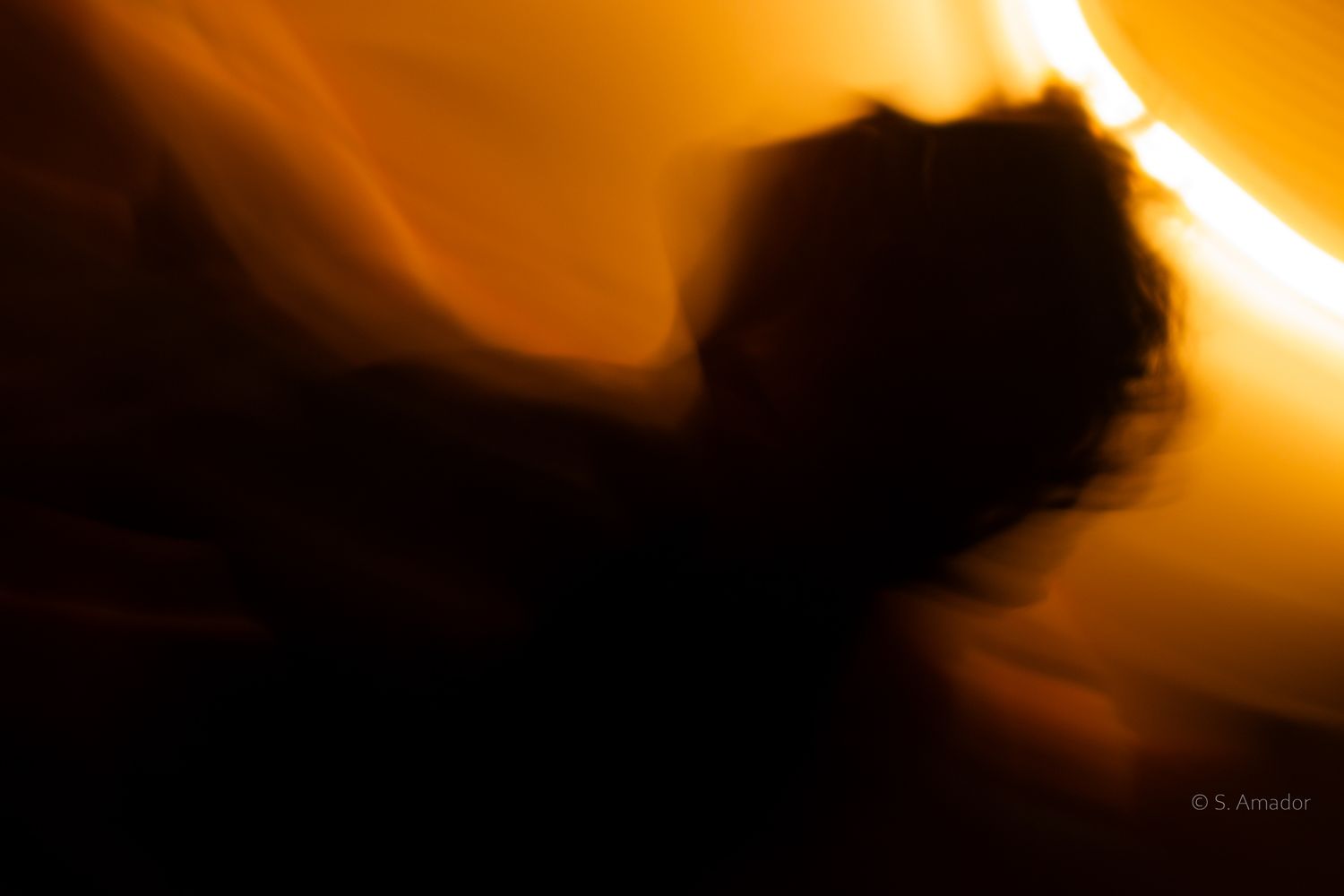 Abstract motion blur portrait bathed in warm golden orange light, creating a dreamy, ethereal silhouette effect.