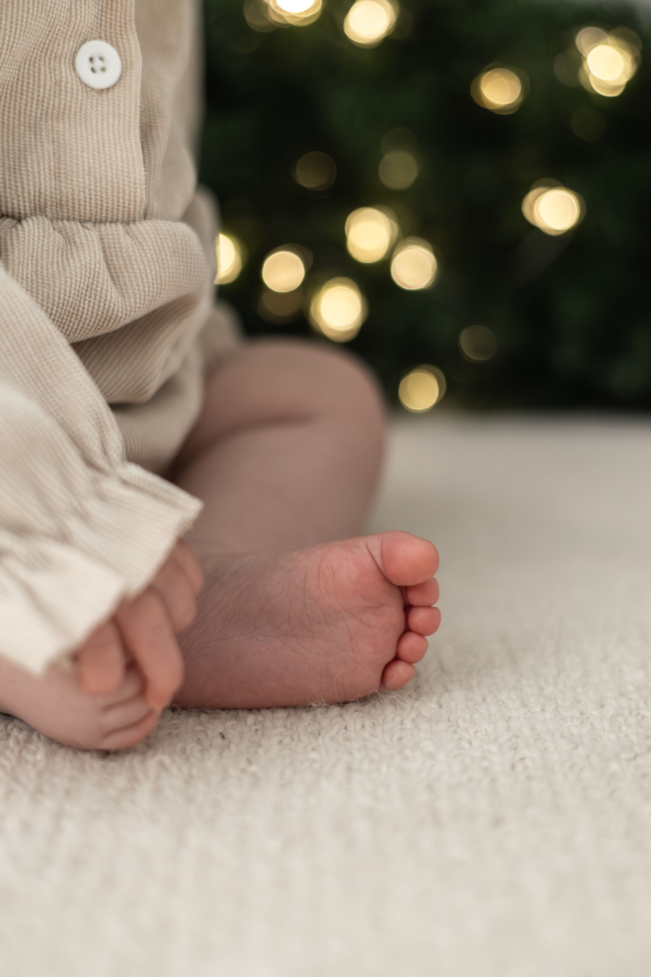 Close-up of tiny baby feet sitting on white carpet in front of a bokeh Christmas wreath warm lights Christmas mini Photoshoot Nottingham