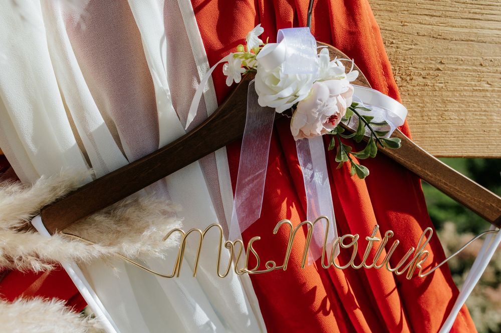Custom Mrs. Matejk wooden wedding dress hanger adorned with white flowers and red bridesmaids dresses.