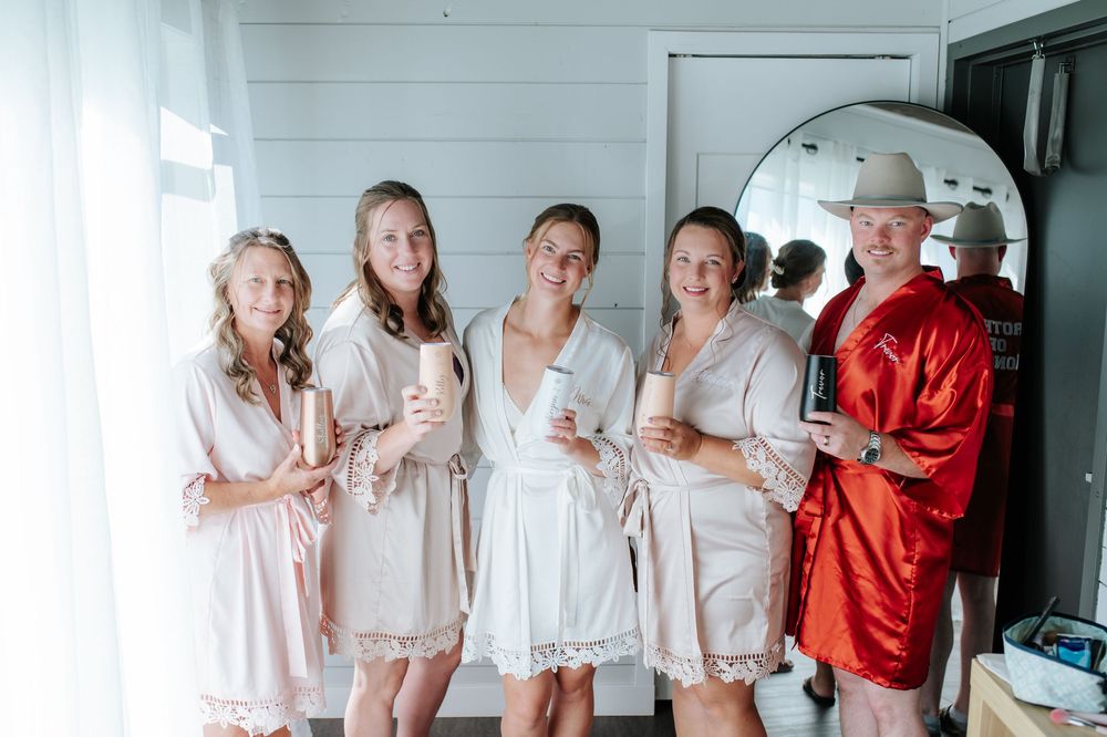 Five bridesmaids in matching robes smile and hold candles while getting ready for a wedding celebration.