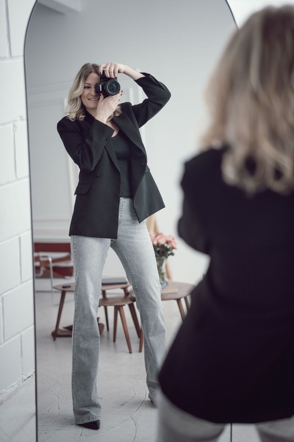 Jacky fotografiert sich mit ihrer Kamera vor einem großen Spiegel in einem Studio.