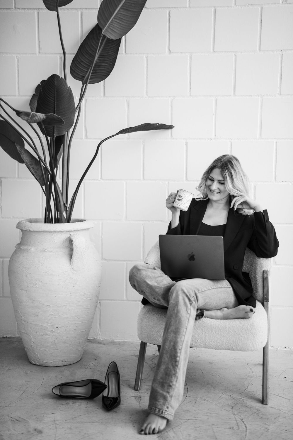 Jacky lächelt mit einer Kaffeetasse am Laptop in einem Schwarz-Weiß-Porträt.